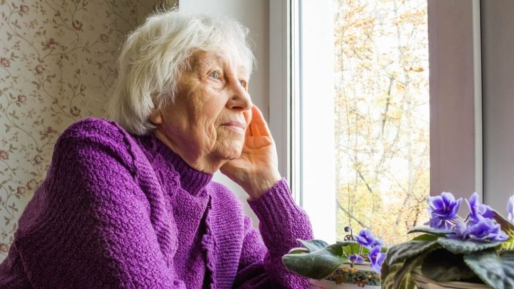 elderly woman in purple sweater looking out window