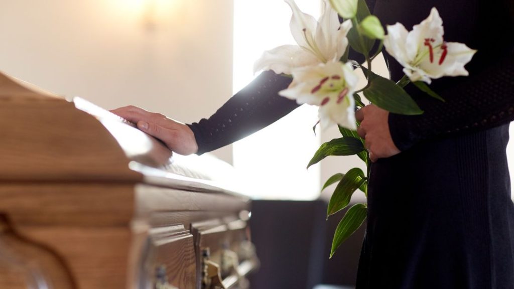 person holding white flowers by casket