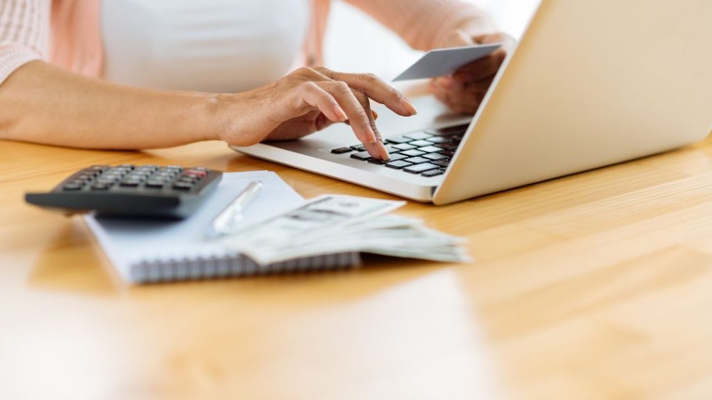 woman working on laptop with calculator, cash, credit card